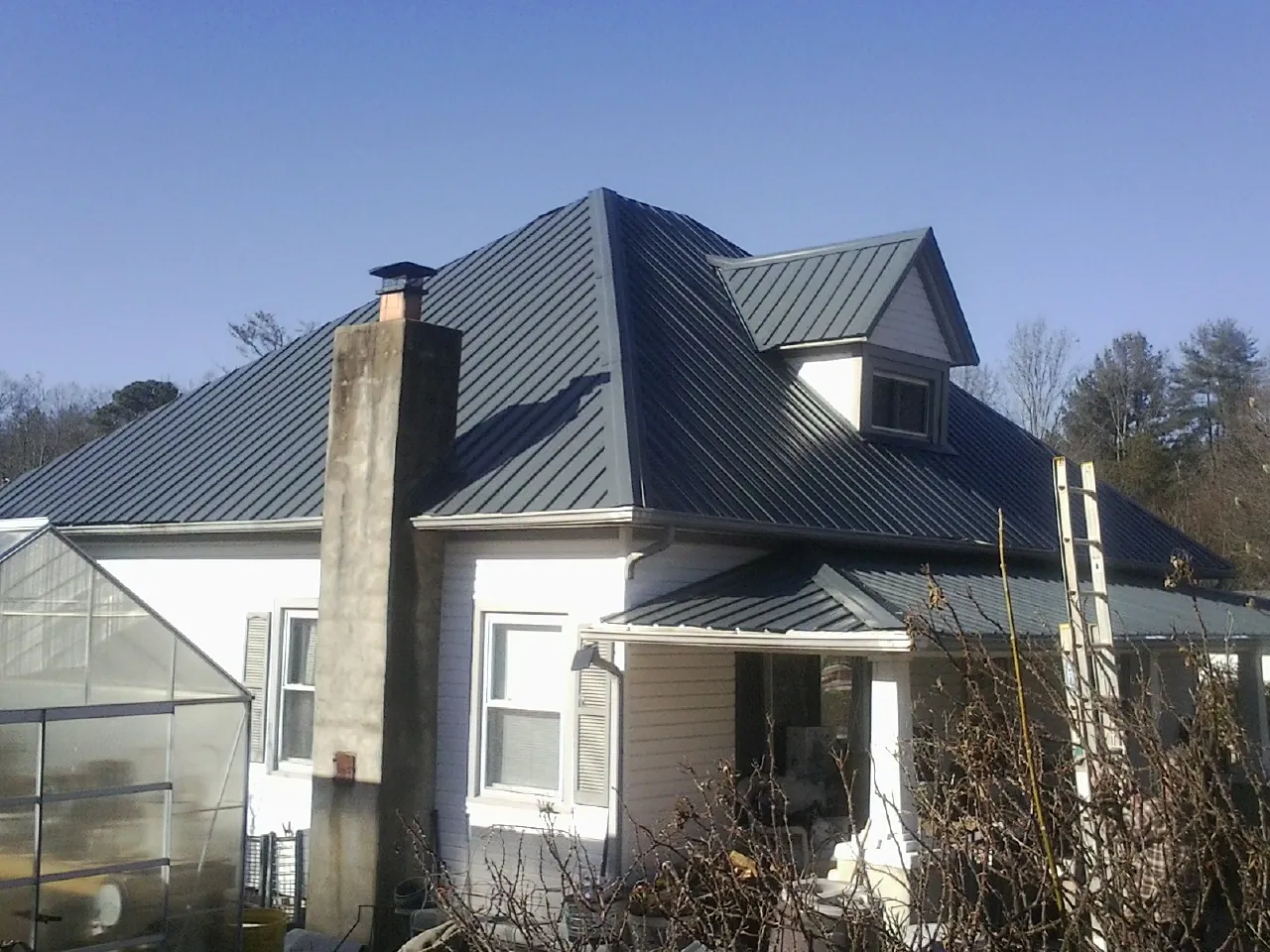 Dark blue standing seam metal roof on a white farmhouse with dormer — Slate & Tile Roof Repair by Roofing Brothers in Westchester