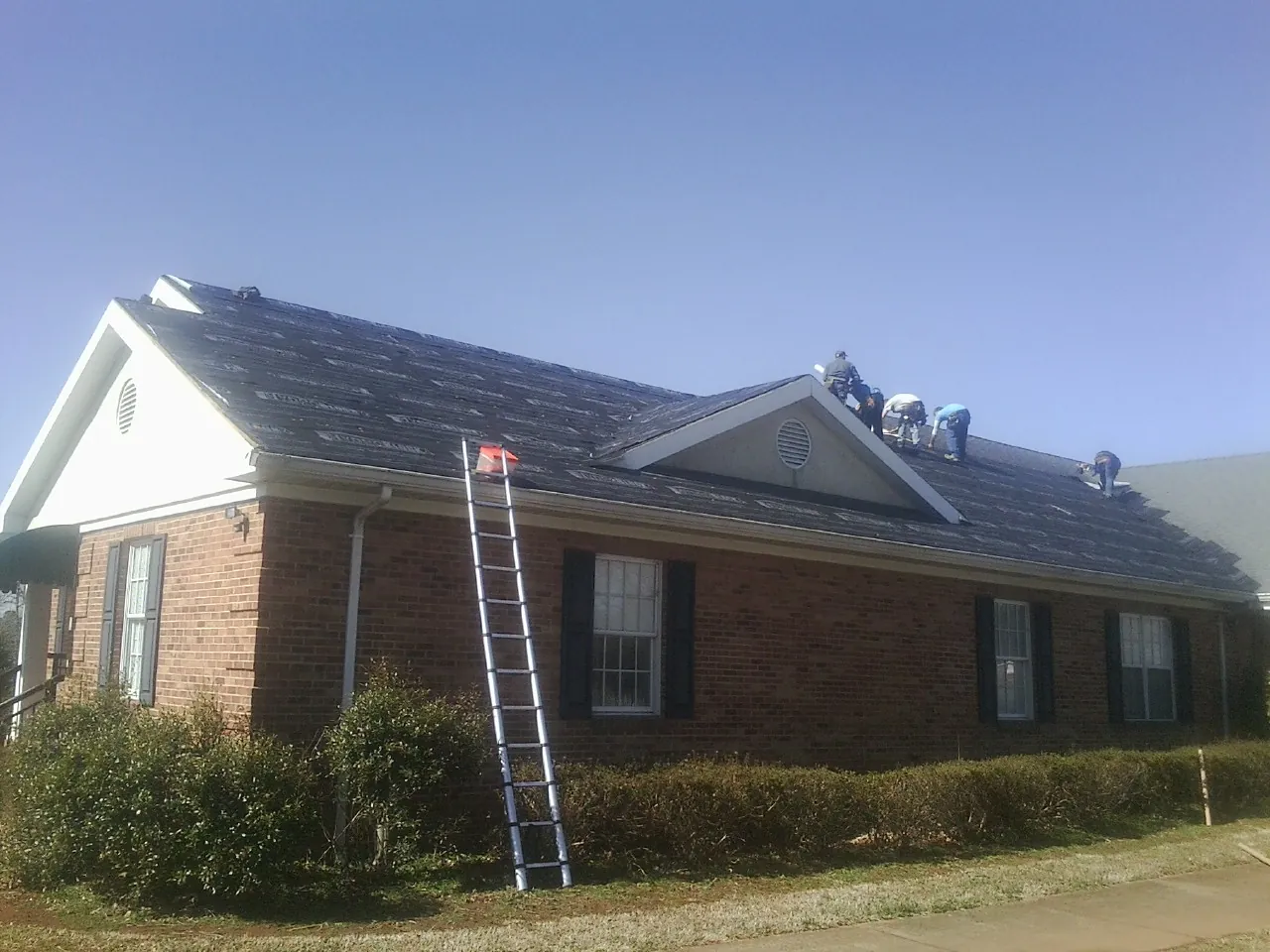 Crew tearing shingles off a brick ranch roof with a ladder set — Emergency Roof Repair work by our crew in Westchester