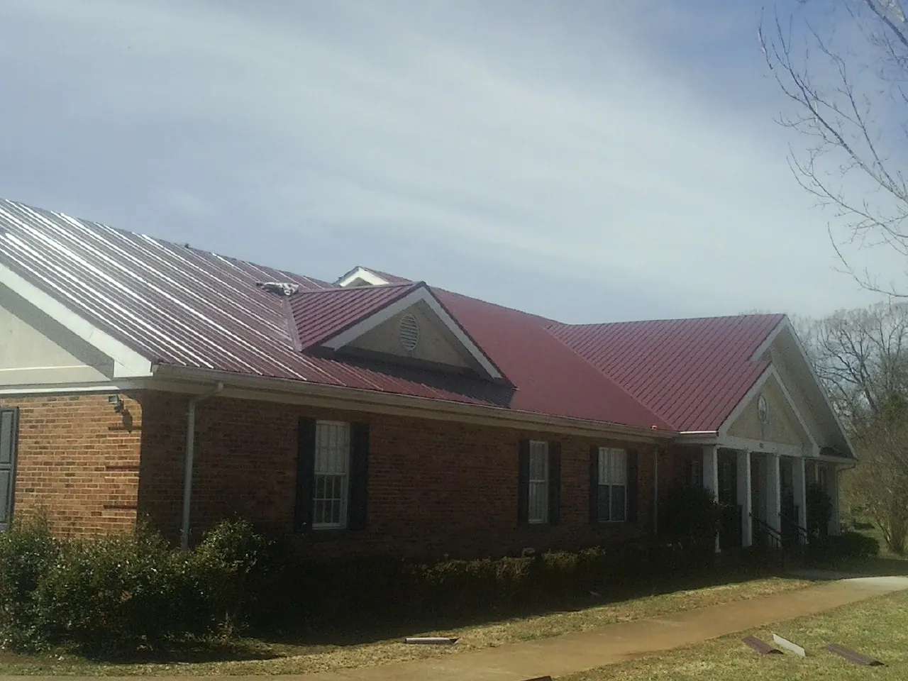 Red metal roof with gabled entries on a long brick building, from a Hail Damage Roof Repair job in Westchester