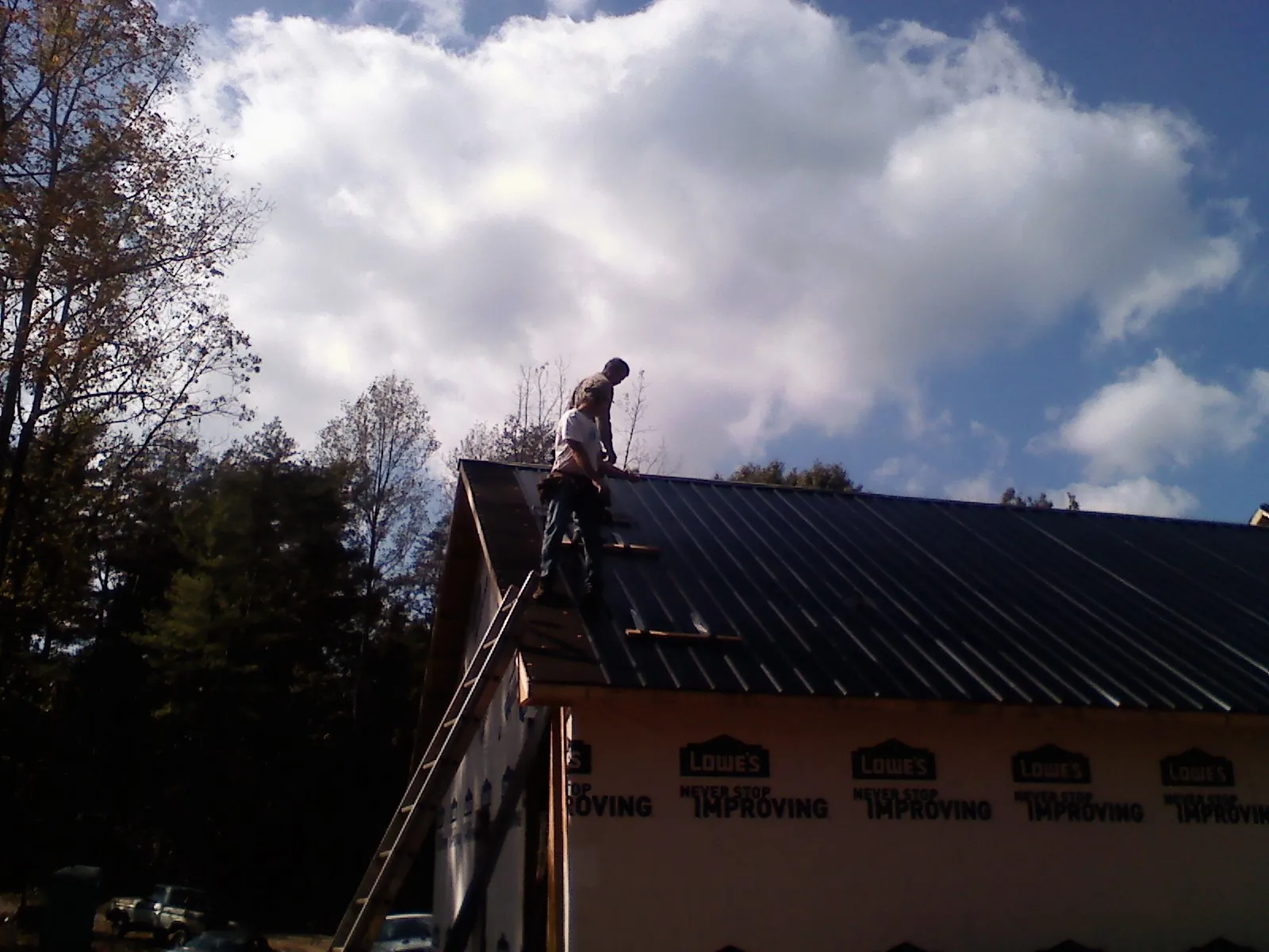 Roofer fastening dark metal panels high against a cloudy sky, from a Roof Inspection job in Westchester