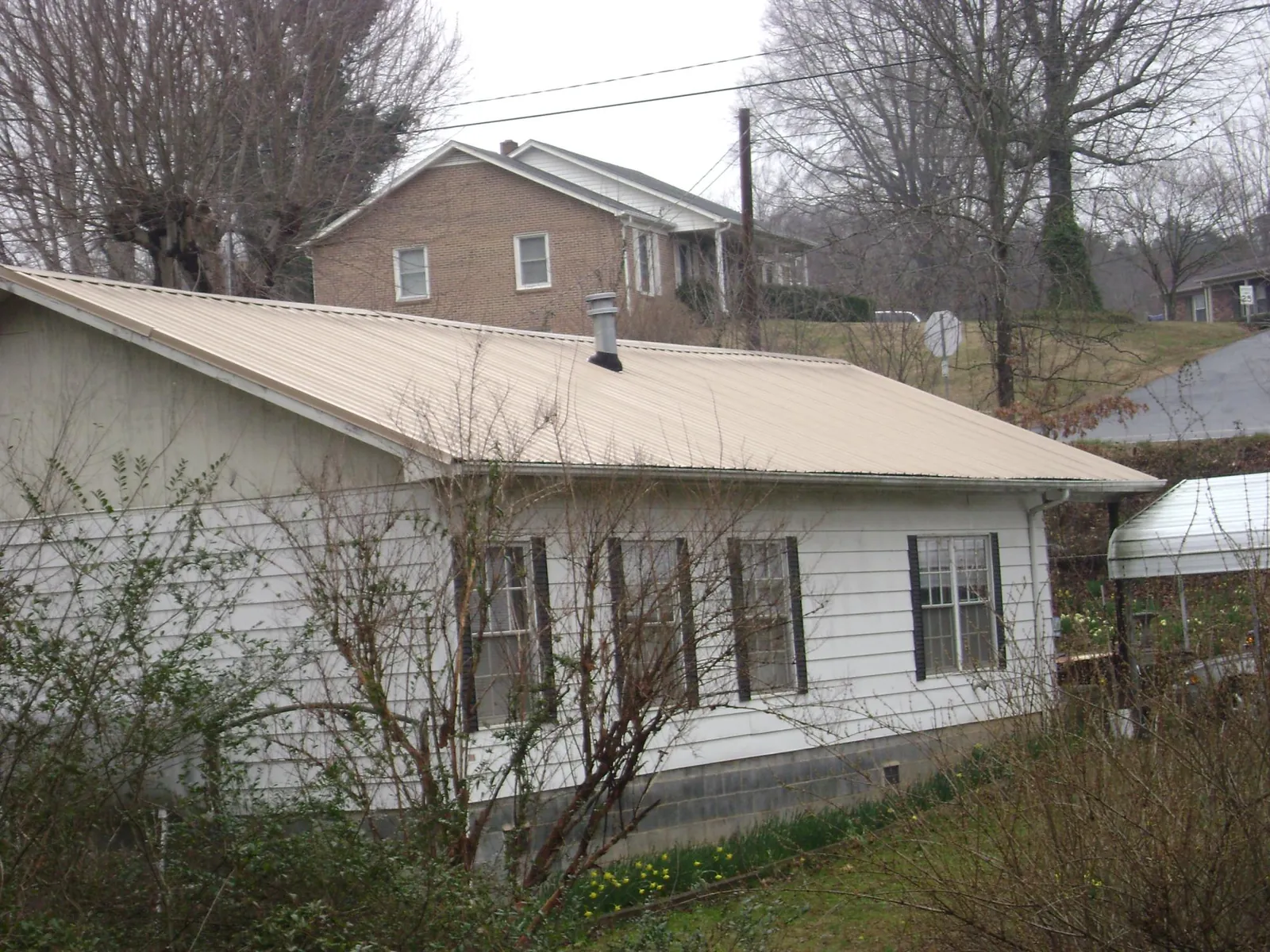 Tan metal roof on a white sided house set into a hillside — Commercial Roofing by Roofing Brothers in Westchester
